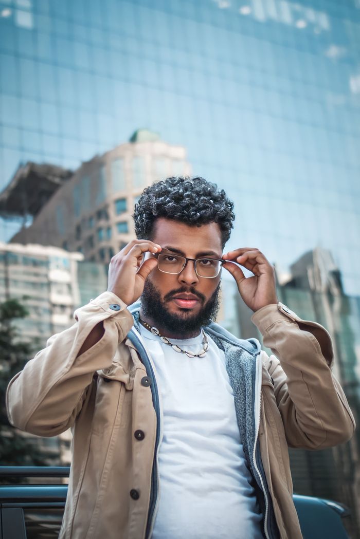 Portrait of a stylish man adjusting glasses with city buildings reflection in the background.