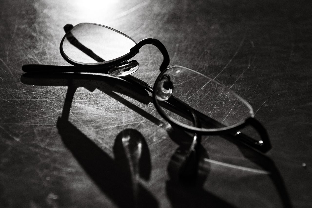 Black and white photo of eyeglasses with shadow on a reflective surface.