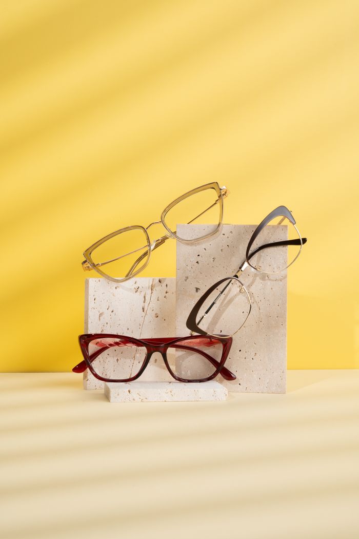 Stylish eyeglass frames showcased on textured blocks with a vibrant yellow backdrop.